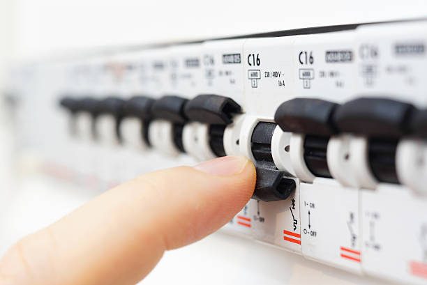 A person's finger is flipping a switch on an electrical circuit breaker panel.